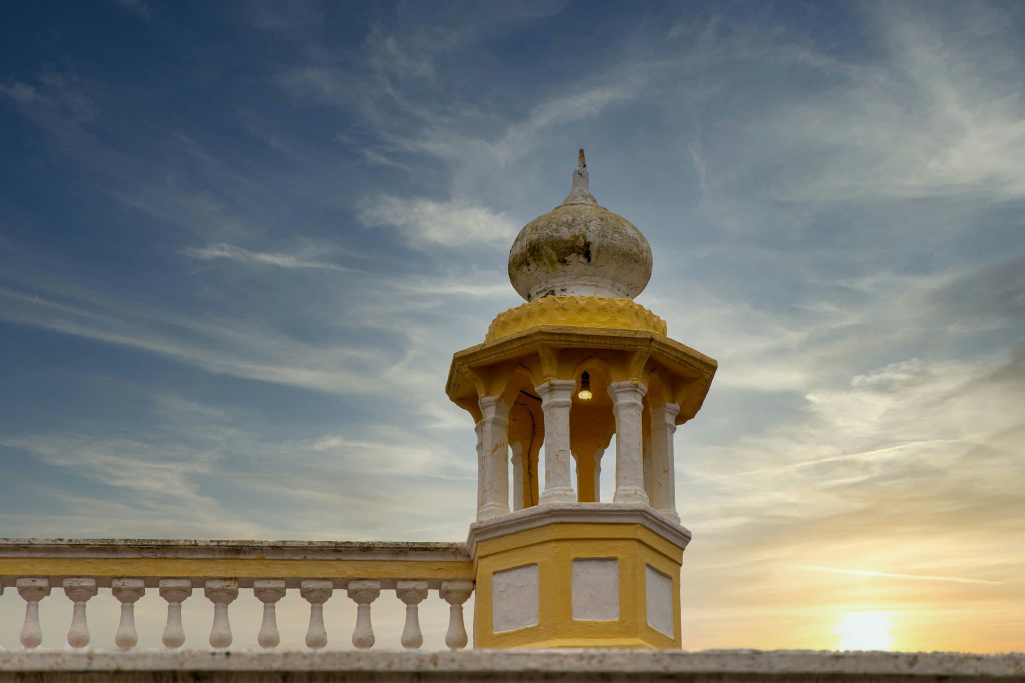 A white and gold domed cupola on a terrace balustrade against a sunset sky, Karnataka