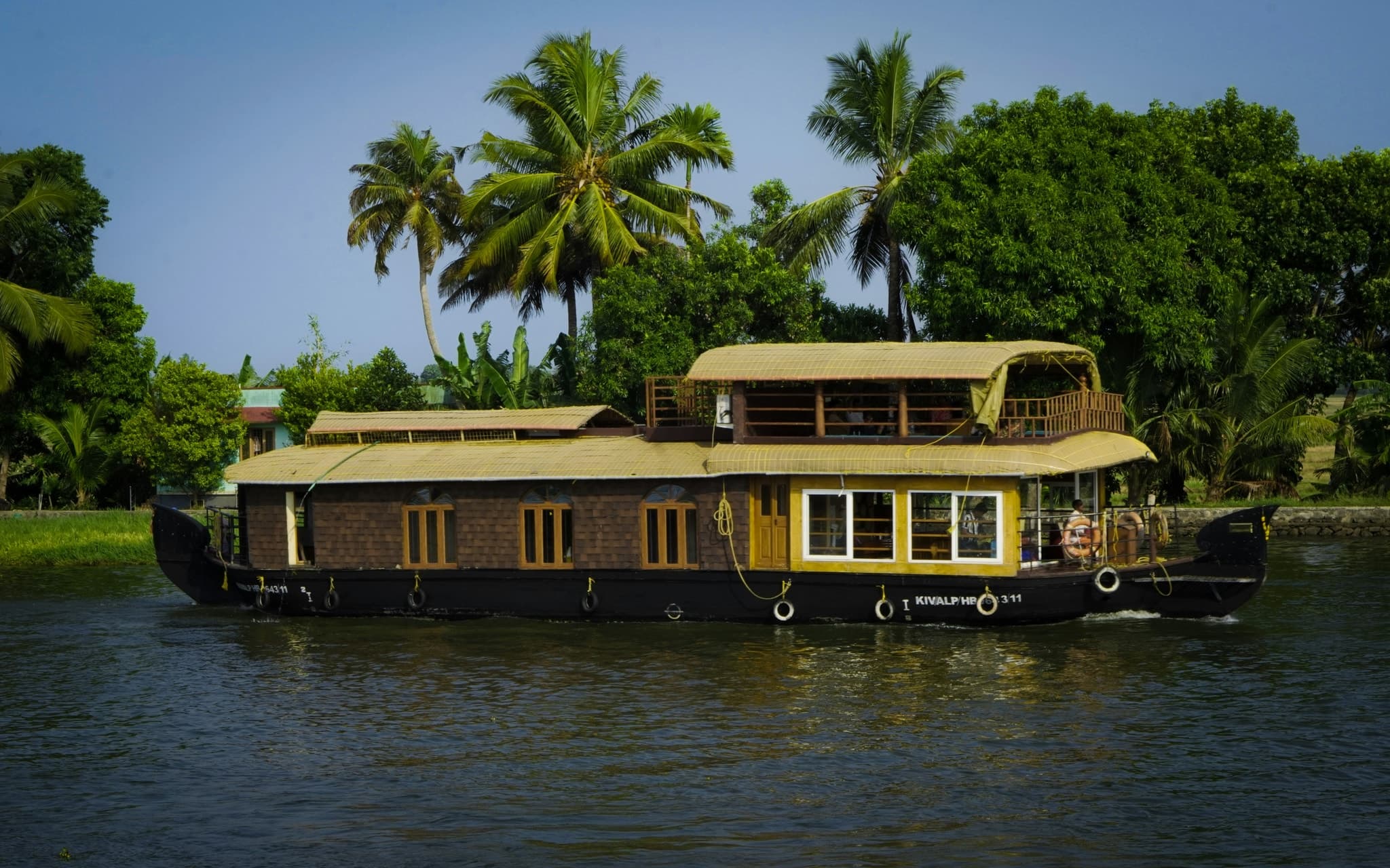 A thatched houseboat on the Alleppey backwaters with coconut palms along the bank, Kerala