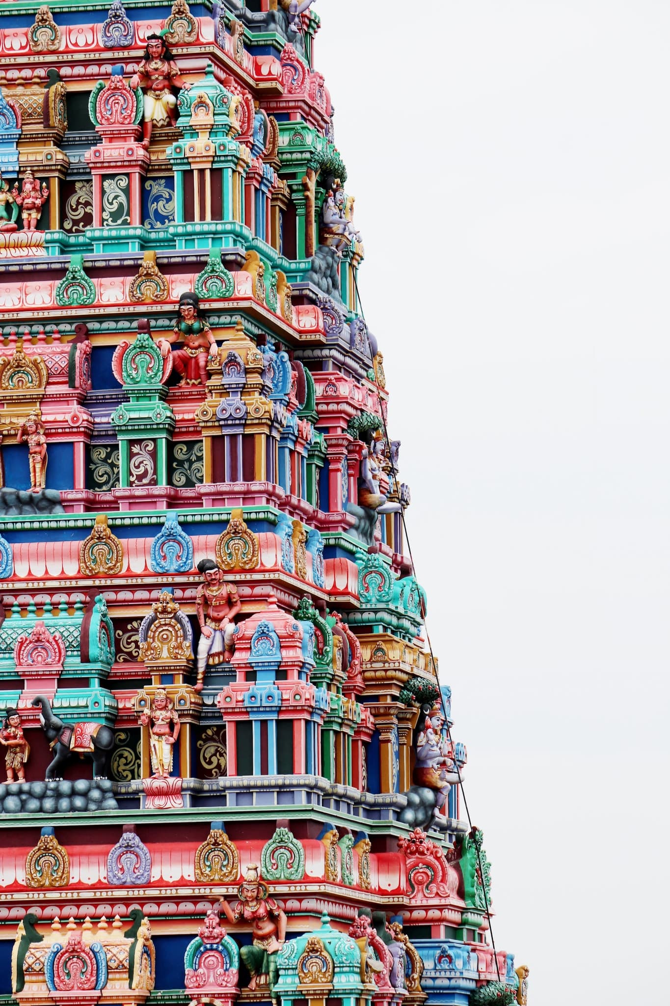 The brightly painted carved tiers of a temple gopuram rising against a pale sky, Tamil Nadu